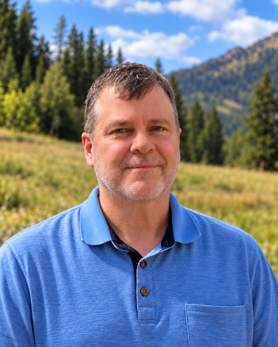 Troy E. Kirk in a blue shirt, with forested mountains behind him